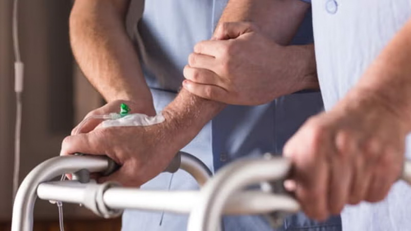 A nurse assists a patient with a walker, providing support during mobility.