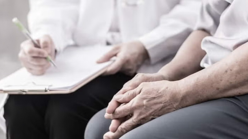 Doctor taking notes on a clipboard while a patient waits in an office.