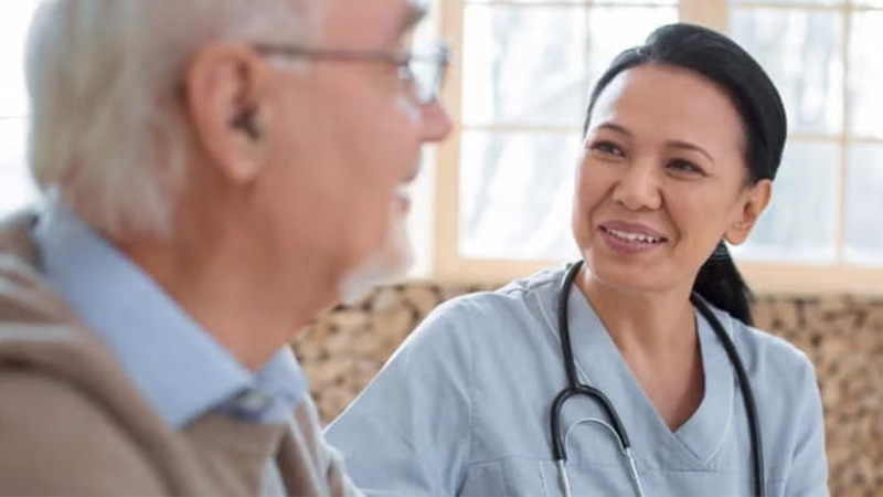 A healthcare professional smiling while talking to an elderly patient.