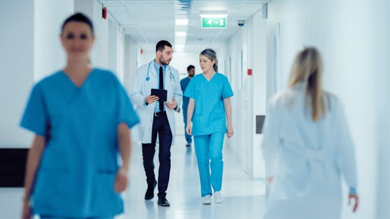Medical professionals in scrubs walking through a hospital hallway.
