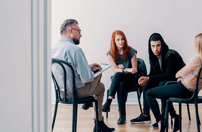 A therapist leads a group counselling session with three young adults.