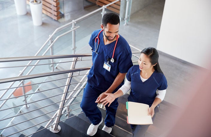 Two nursing students in scrubs walking up a staircase while talking.