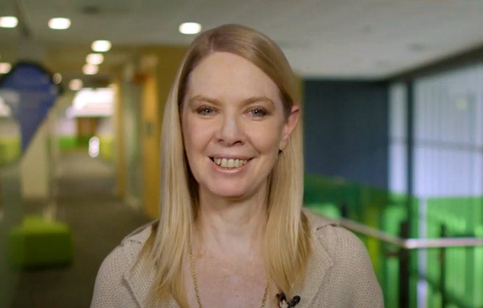 A woman with long blonde hair in a hallway setting.