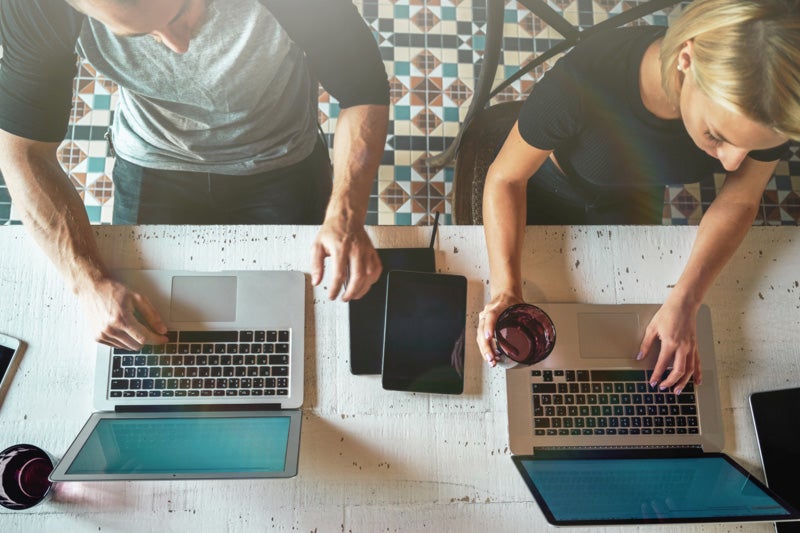 Top-down view of two people using laptops and drinking coffee in a cafe-style workspace.